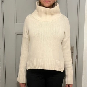 Vit polotröja  - Säljer en vit polotröja med hög krage och ribbade muddar. Tröjan är stickad och har långärmad design med lite loose passform. Perfekt för att hålla sig varm och snygg under kyliga dagar.