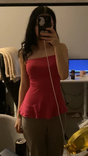 Rosa tubtopp med volang - Säljer en snygg rosa tubtopp med volangkant nedtill. Toppen är axelbandslös och har en figurnära passform som framhäver midjan. Materialet känns mjukt och stretchigt, perfekt för dig som gillar att sticka ut med färg.