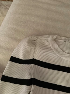 Vit och svart randig tröja från ONLY - Säljer en ribbad vit tröja från ONLY med svarta horisontella ränder. Tröjan har rund hals, puffade axlar och långa ärmar. Materialet är mjukt och stretchigt, perfekt för dig som gillar en clean och stilren look med lite edge.
