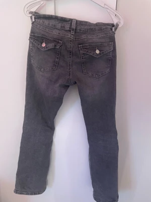 Grå jeans från Gina Tricot, storlek 158 - Snygga grå jeans från Gina Tricot i storlek 158. Klassisk femficksmodell med raka ben och silverfärgade knappar på bakfickorna. Jeansen har bälteshällor och dragkedja framtill. Perfekt för dig som gillar en enkel och stilren look.