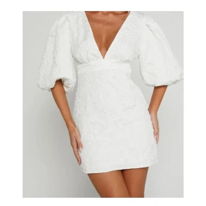 Vit kort klänning med puffärmar/ studentklänning - Superfin vit kort klänning med djup v-ringning och stora puffärmar. Klänningen har markerad midja och strukturmönstrat tyg som ger en lyxig känsla. Perfekt för student eller sommarens alla tillfällen. Sitter snyggt och känns riktigt trendig!