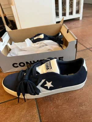 Converse CONS blåvita sneakers - Snygga Converse CONS sneakers i mörkblå mocka med vita detaljer och vit sula. Klassisk stjärnlogga på sidan, grova mörkblå skosnören och vit plös med tydlig logotyp. Perfekta för dig som gillar streetstyle och vill ha en ikonisk look.