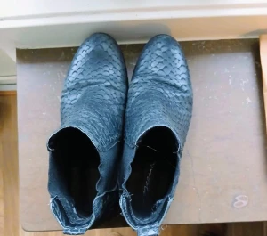 Svarta boots med ormskinnsmönster - Säljer ett par svarta boots med coolt ormskinnsmönster och spetsig tå. Skorna har elastiska paneler på sidorna för enkel påtagning och är tillverkade i ett material som liknar skinn. Perfekta för dig som vill sticka ut med din stil.