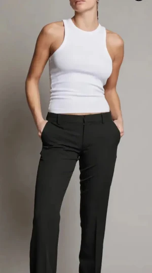 Svarta kostymbyxor med bootcut - Snygga svarta kostymbyxor med klassisk bootcut-passform. Byxorna har pressveck, hällor för bälte och stängs med dragkedja och knapp. Perfekta för en clean och stilren look. Materialet känns mjukt och följsamt.