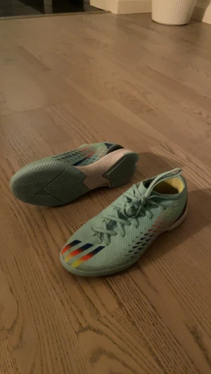 Adidas futsalskor - Säljer ett par mintgröna Adidas futsalskor med snörning och platt sula. Skorna har coola färgdetaljer i blått, rött och gult på sidan och meshmaterial för extra ventilation. Perfekta för dig som vill sticka ut på planen med stil och komfort. Väldigt fina och fräscha. Storlek 36 😁