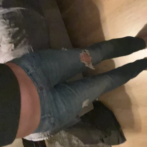Blå ripped jeans från Stocker - Säljer ett par blå jeans från Stocker med snygga slitningar och hål på benen för en cool, avslappnad vibe. Modellen är slim och har klassisk femficksdesign med knapp och dragkedja. 
