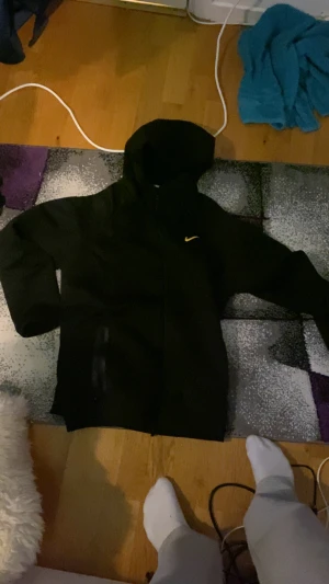 Svart NOCTA x Nike hoodie med dragkedja - Svart hoodie från NOCTA x Nike med gul logga på bröstet och detaljer på ärmen. Tröjan har huva, hel dragkedja Snygg  perfekt för chill dagar.  XL men passar  L