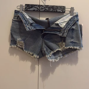  jeansshorts Madden Girl - Snygga jeansshorts från Madden Girl i klassisk blå denim. Modellen har fransiga kanter och slitna detaljer framtill för en cool, avslappnad vibe. Shortsen har dragkedja och knapp, samt bakfickor. Perfekta för sommarens alla äventyr!