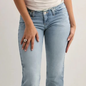 Ljusblå jeans med rå kant från Nelly - Säljer ett par ljusblå jeans från Nelly med fransad kant i midjan och vid benslut. Jeansen har klassisk femficksdesign,  i bootcut och normal passform. 