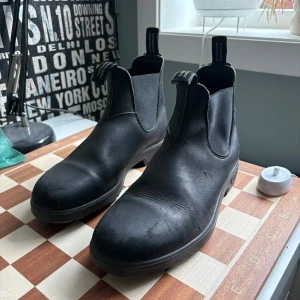 Svarta Blundstone chelsea boots i skinn - Klassiska svarta chelsea boots från Blundstone i äkta skinn. Snygg och tidlös design med elastiska paneler på sidorna och dragflikar med Blundstone-logga. Perfekta för dig som vill ha en robust och stilren sko till vardags.