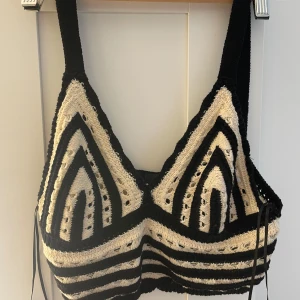 Svartvit stickad croppad topp Gina Tricot - Säljer en croppad stickad topp från Gina Tricot i svart och vitt. Toppen har breda axelband, coolt grafiskt mönster med ränder och håldetaljer, samt snörning i sidorna. Perfekt för att ha över bikini eller klä upp på utlandssemestern☀️🫶