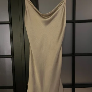 Champagnefärgad klänning Gina Tricot - Säljer en elegant klänning från Gina Tricot i champagnefärgad satin. Klänningen har smala axelband, draperad urringning och en slinky, glansig finish som ger en lyxig känsla. Perfekt för dig som vill sticka ut med en stilren look.
