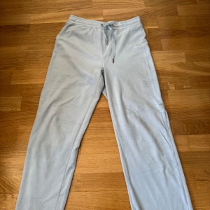 Ljusgrå mjukisbyxor med snörning - Säljer ett par ljusgrå mjukisbyxor med dragsko i midjan. Byxorna har en relaxed fit och är perfekta för chill dagar. Tillverkade i mjukt material som känns skönt mot huden. Enkla att matcha med hoodie eller t-shirt.