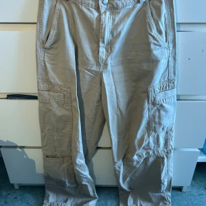 Beiga cargobyxor från H&M - Säljer ett par beiga cargobyxor från H&M i storlek 36. Byxorna har flera stora fickor på sidorna och baktill, raka ben och klassisk cargostil. Perfekta för en avslappnad och trendig look. Materialet är mjukt och bekvämt bomullstyg.