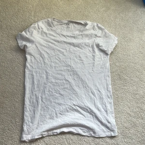 Vit basic t-shirt från 157 - En klassisk vit t-shirt från 157 i 100% bomull. Modellen är enkel med rund halsringning och korta ärmar, perfekt att matcha med jeans eller shorts. T-shirten har en normal passform och är supermjuk mot huden.