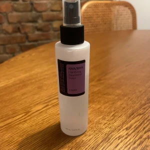 COSRX AHA/BHA Clarifying Treatment Toner - En genomskinlig plastflaska med svart spraymunstycke, innehållande COSRX AHA/BHA Clarifying Treatment Toner. Tonern är 150 ml och har en lila etikett framtill. Perfekt för dig som vill ha en exfolierande toner med mild formula och sprayfunktion. Står under flaskan att den gick ut i början av 2025 men tror ej de ska ha jättestor betydelse 