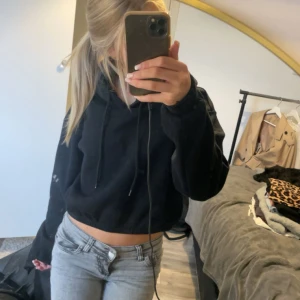 Svart magtröja hoodie  - Svart croppad hoodie från H&M Divided med huva och snörning. Tröjan har långa ärmar med muddar och är i mjuk bomullsblandning. Går inte att köpa längre.