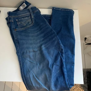 Replay Anbass slim jeans blå - Säljer ett par Replay Anbass slim fit jeans i klassisk blå tvätt. Jeansen har fem fickor, snygga detaljer på bakfickorna och smal passform. Tillverkade i stretchig bomullsdenim för extra komfort. Perfekta för dig som gillar en modern och stilren look.