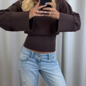 Brun stickad tröja med vida ärmar - Säljer en brun stickad tröja med croppad passform och vida, långa ärmar. Tröjan har en tight midja som ger en snygg siluett och är perfekt för dig som gillar trendiga och stilrena plagg. Helt ny med lapp kvar, enbart provad💕 Skriv om du vill ha egna bilder på hur den sitter på! 