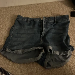 Blå jeansshorts från Divided, strl 44 - Snygga blå jeansshorts från Divided i storlek 44. Klassisk femficksmodell med uppvikta benslut och dragkedja framtill. Perfekta för en avslappnad look och passar till det mesta. Gjorda i slitstarkt jeanstyg med två stora bakfickor.