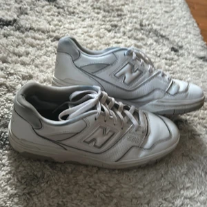 Vita New Balance 550 sneakers - Snygga vita New Balance 550 sneakers med klassisk siluett och lågt skaft. Skorna har tydliga NB-loggor på sidorna och bak, samt snörning framtill. Ovandelen är i skinn med perforerade detaljer och robust sula för extra komfort.