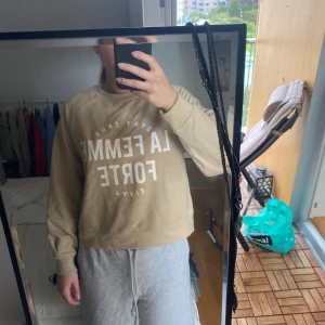 Beige sweatshirt från Etirel - Säljer en beige sweatshirt från Etirel i storlek M. Tröjan har trycket 'LA FEMME FORTE' i vitt framtill, rund hals och långa ärmar. Skön och avslappnad passform, perfekt till chill dagar. Materialet är mjukt och känns som bomull.