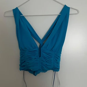 Turkos omlott croppad topp - Snygg turkos croppad topp med omlott-design och djup v-ringning. Toppen har rynkade detaljer framtill. Perfekt för dig som vill sticka ut med en färgstark look. Aldrig använd! Från Zara.