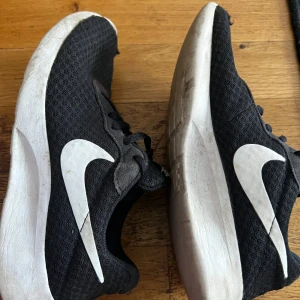 Svarta Nike sneakers med vit sula - Svarta Nike sneakers med vit sula och stort vitt Swoosh på sidorna. Ovandelen är i mesh för bra andningsförmåga och skorna har klassisk snörning. Perfekta för dig som gillar en sportig och clean look.