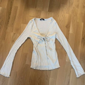 Vit omlottopp med knyt från Bik Bok - Supersöt vit omlottopp från Bik Bok i ribbad bomullsmix. Toppen har lång ärm, v-ringning och knyt framtill som ger en feminin touch. Aldrig använd 💗#bikbok