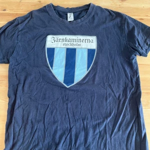 Blå Järnkaminerna t-shirt  - Mörkblå t-shirt från SOL'S med stort Järnkaminerna Stockholm-tryck på bröstet i blå och ljusblå nyanser. Klassisk rund hals och korta ärmar. Skön bomullskvalitet, perfekt för dig som vill visa ditt stöd för laget.