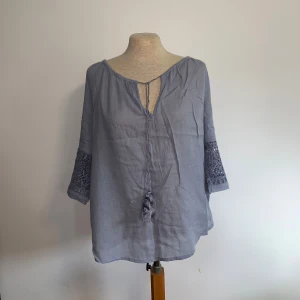 Två boho inspirerade tröjor  - Luftig blå blus från Indiska i linne med snygga spetsdetaljer på ärmarna och knytband med tofs framtill. Blusen har trekvartsärm och en avslappnad passform, perfekt för en chill och bohemisk stil, storlek M. Mörkblå kofta från Kappahl, storlek one size