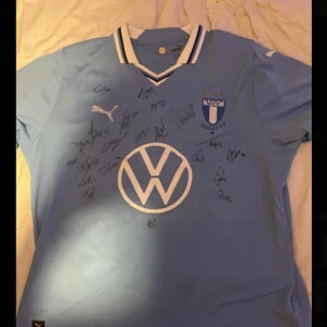 Malmö FF matchtröja Puma signerad - Säljer en ljusblå Malmö FF fotbollströja Storlek L från Puma med klubbmärke, VW-logga och flera autografer på framsidan. Taha alis atougraf finns med. Tröjan har korta ärmar och klassisk V-ringning med vit och svart detalj. Perfekt för dig som älskar fotboll och samlar på supporterprylar.