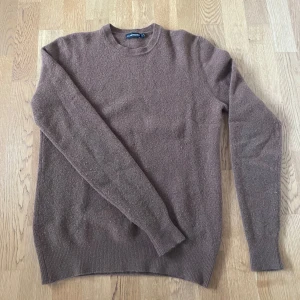 J.Lindeberg ulltröja - Säljer en brun stickad tröja från J.Lindeberg i storlek M. Materialet är mjuk ull som värmer bra under kyligare dagar. Finns lite noppor på tröjan, men övrig i väldigt fint skick. Om det finns frågor eller behövs fler bilder, tveka inte på att höra av dig! 
