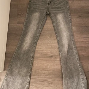Grå bootcut jeans med tvättad look - Säljer ett par grå jeans med snyggt tvättad effekt och bootcut-modell. Jeansen har klassisk femficksdesign och raka sömmar. Perfekta för dig som gillar en retrostil med lite extra vidd nertill. Passar till sneakers eller boots.