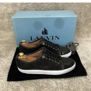 Svarta sneakers från Lanvin i mocka - Snygga svarta sneakers från Lanvin med ovandel i mocka och lackad tå. Skorna har vita sulor, svarta skosnören och silverfärgade öljetter. Perfekta för dig som gillar stilrena och exklusiva sneakers med en twist.