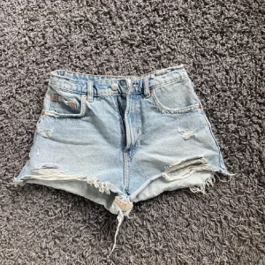 Ljusblåa highwaist jeansshorts - Snygga ljusblå jeansshorts med hög midja och slitna detaljer. Klassisk femficksmodell med råa kanter och fransar nertill. Perfekta för sommardagar och festivalhäng.