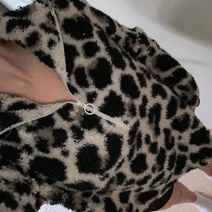 Jättefin Leopardmönstrad fleecehoodie Firefly L - Säljer en supermjuk och fluffig hoodie från Firefly i storlek L. Tröjan har leopardmönster i svart och beige, dragkedja med vit rund detalj och huva. Perfekt för kalla dagar när du vill vara både varm och snygg.