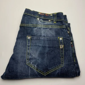 Dondup jeans  - Snygga blå dondup jeans med markerade gula sömmar och klassisk femficksdesign. Jeansen har coola detaljer som nitar och logga på bakfickan. Perfekta för dig som gillar en streetig och avslappnad look.