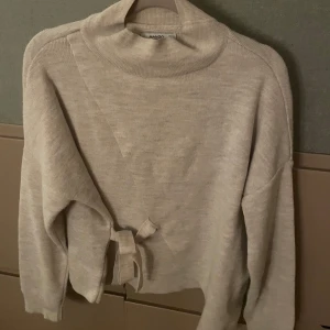 Beige stickad tröja med knyt från Mango - Beige stickad tröja från Mango med hög krage och snygg knytning i sidan. Tröjan är i ullblandning, super skönt och varmt till hösten och vintern!💞