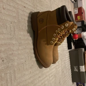 Timberland boots i beige mocka - Säljer ett par klassiska Timberland boots i beige mocka med bruna detaljer och gul snörning. Skorna har grov sula, rund tå och vadderad kant runt ankeln för extra komfort. Perfekta för höst och vinter, riktigt snygga till streetwear. Pris kan diskuteras 