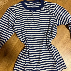 Randig långärmad tröja i blått och vitt - Säljer en klassisk långärmad tröja med blå och vita ränder. Köpenhamn och Stockholm stil! Tröjan har rund halsringning och muddar i blått vid ärmslut och hals. Perfekt för dig som gillar en tidlös och chill stil. Materialet känns mjukt och skönt mot huden. Nytt skick