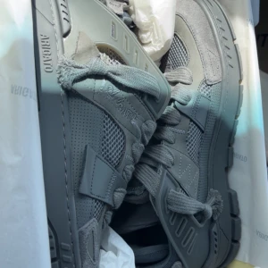 Grå sneakers från Axel Arigato - Säljer ett par grå sneakers från Axel Arigato med coola detaljer och chunky sula. Skorna har meshpaneler, mocka och skinn samt snörning och robust design. Perfekta för dig som gillar streetstyle och vill ha något som sticker ut. Allt som kom med när jag köpte finns kvar aldrig använda