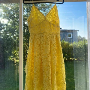 Gul spetsklänning med axelband - Säljer en söt gul klänning med smala axelband och v-ringad hals. Klänningen är kort och har ett vackert blommigt spetsmönster över hela klänningen. Passar XS/S