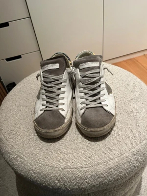 Philippe Model vita och grå sneakers - Säljer ett par Philippe Model sneakers i vitt och grått med detaljer i mocka och skinn. Skorna har snörning, rund tå och en cool camouflagemönstrad häl. Klassisk låg modell med svart sula och diskret logga på sidan.