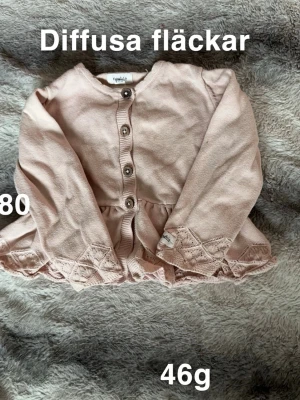 Rosa kofta från Newbie med spets - Söt ljusrosa kofta från Newbie med fina spetsdetaljer längs nederkanten och knappar framtill. Långärmad och perfekt för lager på lager. Passar dig som gillar romantisk och gullig stil.🌸 Diffusa fläckar. Storlek 80