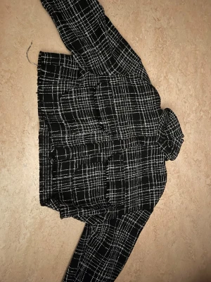 Svartvit rutig tunn jacka  - Säljer en svartvit med rutigt mönster tunn kort jacka. Jackan har två stora fickor framtill och en klassisk krage. Det är storlek M men den är liten i storlek. 