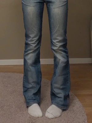 ljusblå bootcut jeans låg midja - Säljer ett par ljusblå jeans med bootcut passform. Jeansen har klassisk femficksdesign, låg midja och snygga "slitningar" framtill och baktill. Materialet är mjukt jeans-tyg och dekorativa sömmar på backfickorna. 
