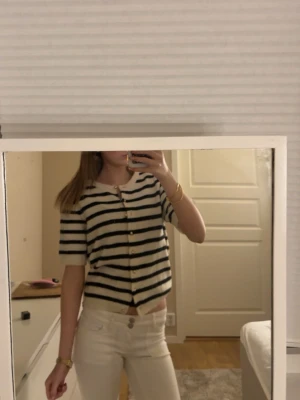 Randig kofta från H&M  - Kortärmad kofta från H&M i vit och svart randigt mönster. Tröjan har rund halsringning, knappar framtill och är stickad i mjuk ullmix. Perfekt för lager på lager och ger en chill men ändå stilsäker vibe.