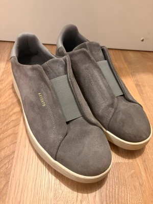 Gråa Axel Arigato sneakers - Snygga grå sneakers från Axel Arigato i mocka med vit sula och diskret guldtext på sidan. Skorna är endast använda ett fåtal gånger!