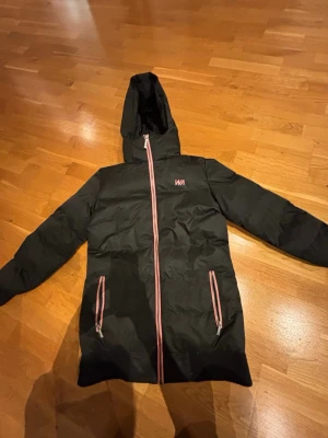 Svart pufferjacka från warp - Svart pufferjacka med rosa dragkedjor. Jackan har två fickor med dragkedja och ett stilrent tryck på bröstet. 